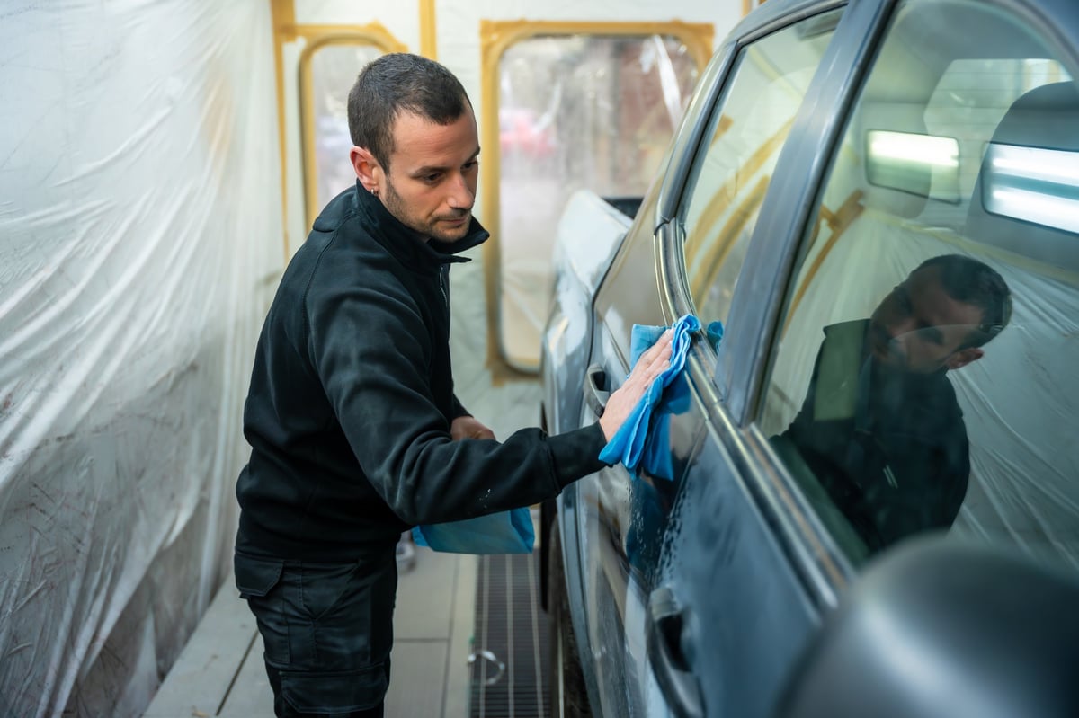 Technician cleaning and prepping a car in a paint booth before painting