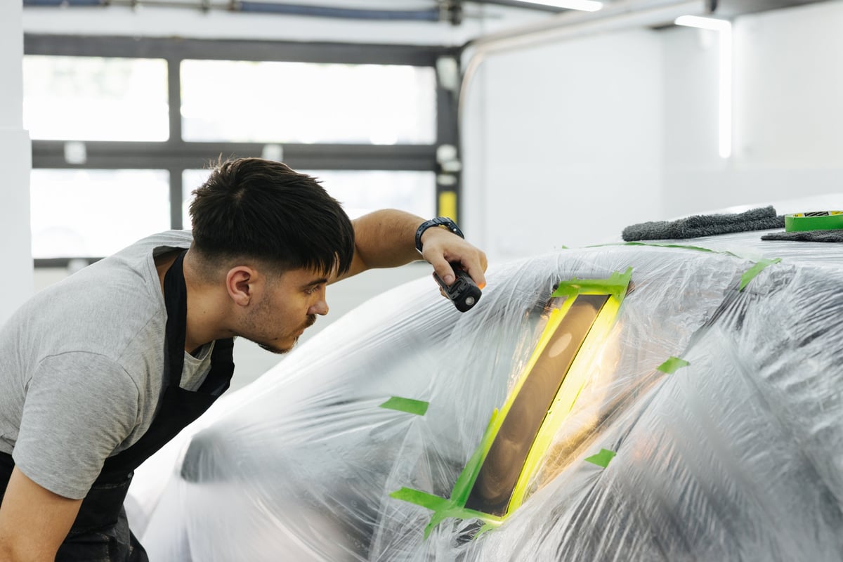 Mechanic polishing a masked car panel during body repair and paint preparation